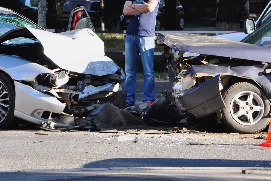 A man with his arms crossed standing next to a two-car head-on collision, which has resulted in a serious accident on the roads in Springfield, IL.