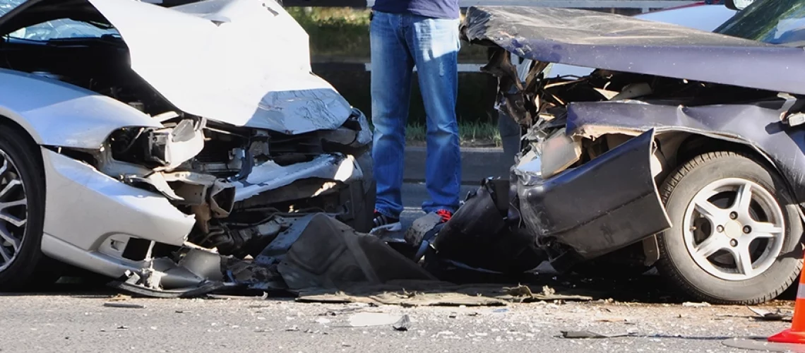 A man with his arms crossed standing next to a two-car head-on collision, which has resulted in a serious accident on the roads in Springfield, IL.